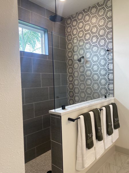 A modern shower featuring hexagonal tiles, a sleek rain showerhead, and a towel rack with dark accents.