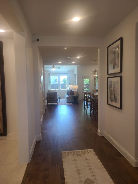 A cozy hallway with wooden floors, elegant framed art, and bright lighting leading to a chic, open living space.