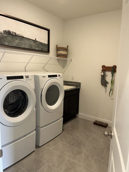 Modern laundry room with a sleek washer and dryer, dark cabinetry, and tasteful wall art. Modern laundry room with a sleek washer and dryer, dark cabinetry, and tasteful wall art.