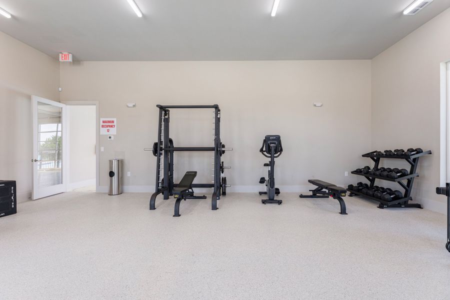 Fitness room with squat rack, stationary bike, weight bench, and dumbbell rack on light speckled floors