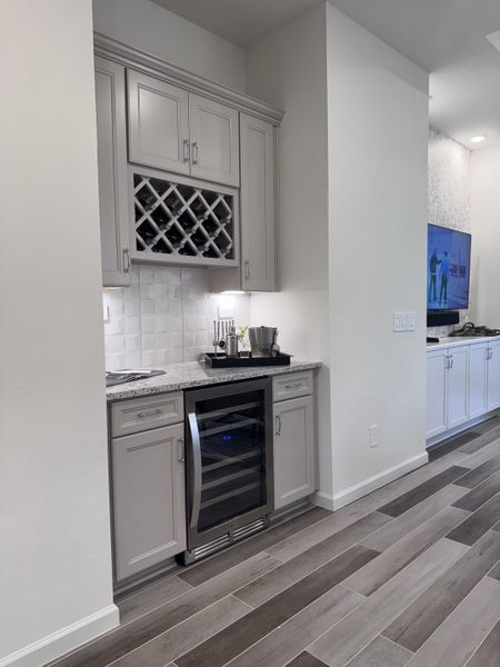 A sleek home bar with a wine rack, granite countertop, and wine cooler, complemented by elegant cabinetry and wood flooring.