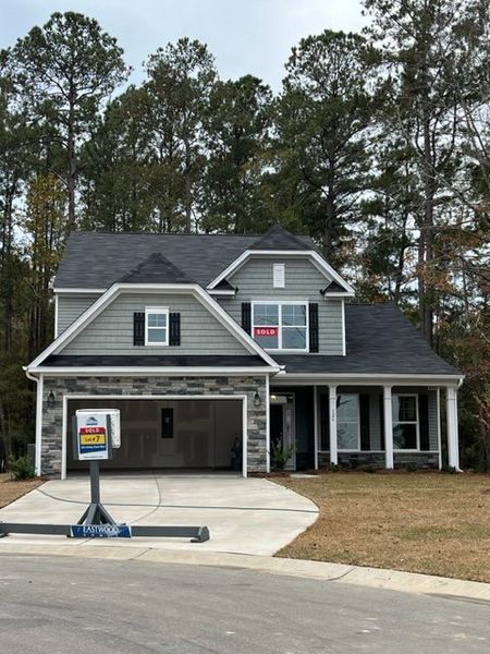 A charming gray home with stone accents and a lush, wooded backdrop in Ashley Cove by Eastwood Homes (Summerville, SC).