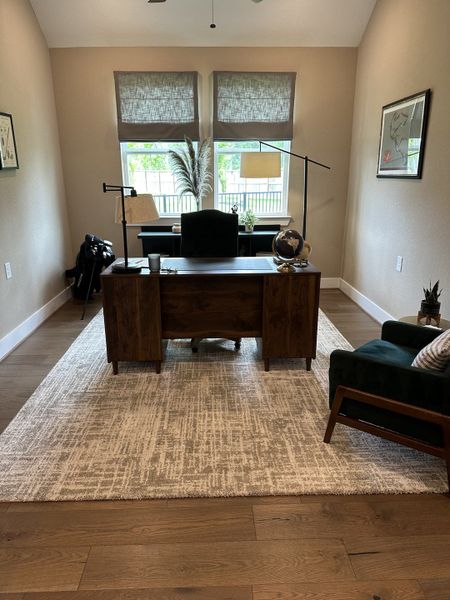 A cozy home office with wood flooring, a sleek desk, modern lighting, and natural light filtering through stylish shades.