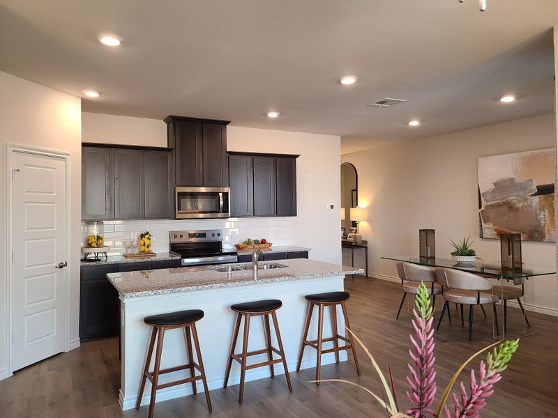 Modern kitchen with dark cabinets, granite island, and wood flooring, opening to a stylish dining area with contemporary decor. Modern kitchen with dark cabinets, granite island, and wood flooring, opening to a stylish dining area with contemporary decor.