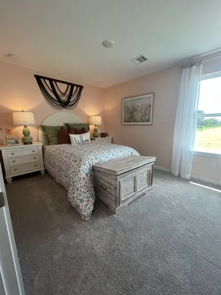A cozy bedroom featuring soft pink walls, a floral bedspread, and elegant decor with ample natural light filtering through windows.