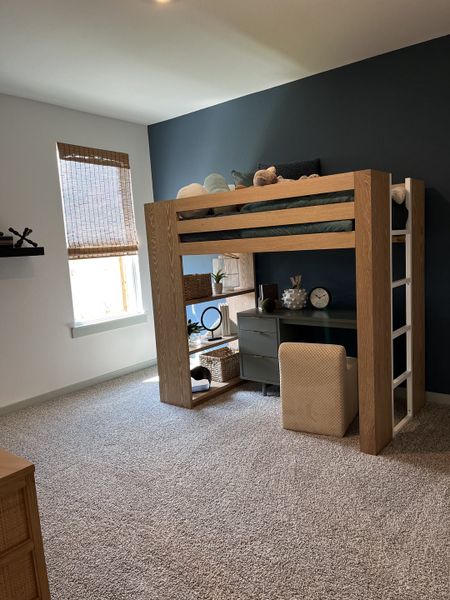 A cozy kids' room with a loft bed, dark accent wall, and functional desk space, accented by natural light and soft carpet.