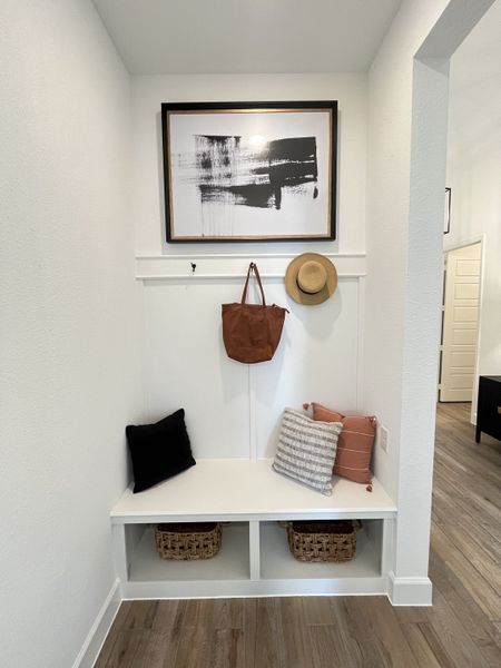 A chic entryway nook with a white bench, abstract art, cozy pillows, and woven baskets for storage. A chic entryway nook with a white bench, abstract art, cozy pillows, and woven baskets for storage.