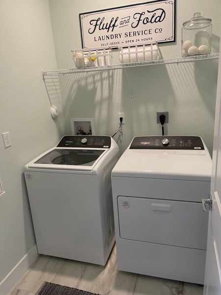 A functional laundry room with modern appliances, decorative sign, and neatly organized shelves.