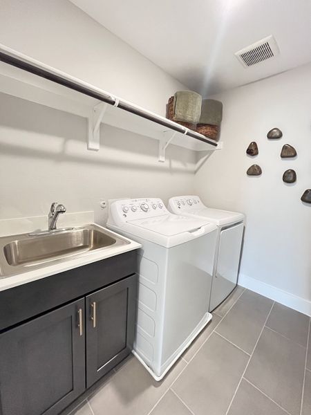A modern laundry room featuring a sleek black cabinet, utility sink, and white appliances on large tile flooring.