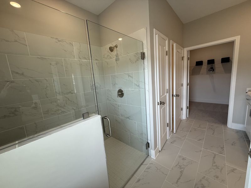 A modern bathroom featuring a glass walk-in shower with marble tiles, a spacious closet, and sleek fixtures.