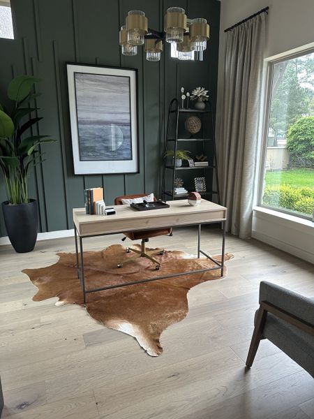 A chic home office with a modern desk, cowhide rug, green panel wall, and elegant art.