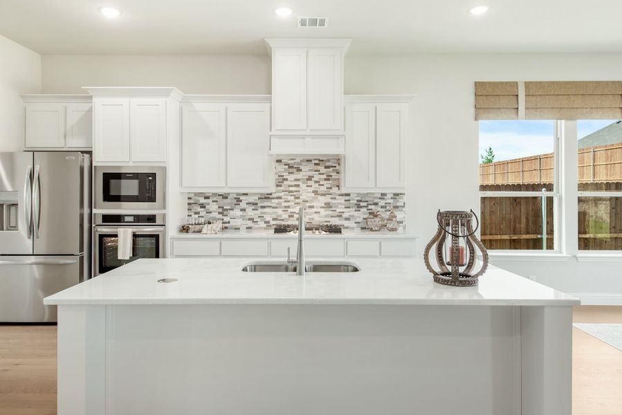 Kitchen with white island and sink, white cabinets, tile backsplash, and stainless steel appliances