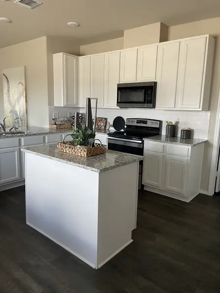 A modern kitchen with sleek white cabinetry, granite countertops, dark wood flooring, and stainless steel appliances.