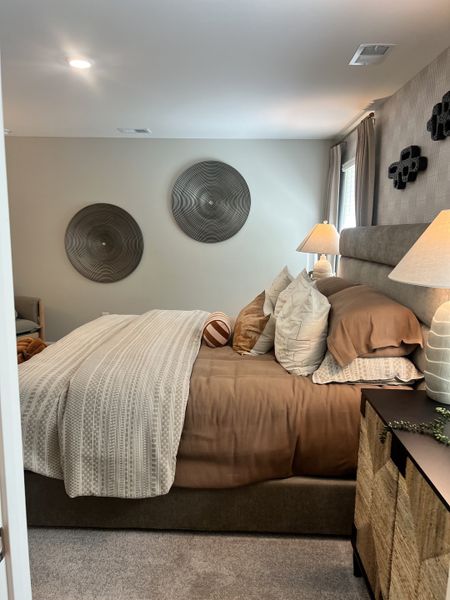 A cozy bedroom featuring earthy tones, textured bedding, and elegant wall decor with soft ambient lighting.