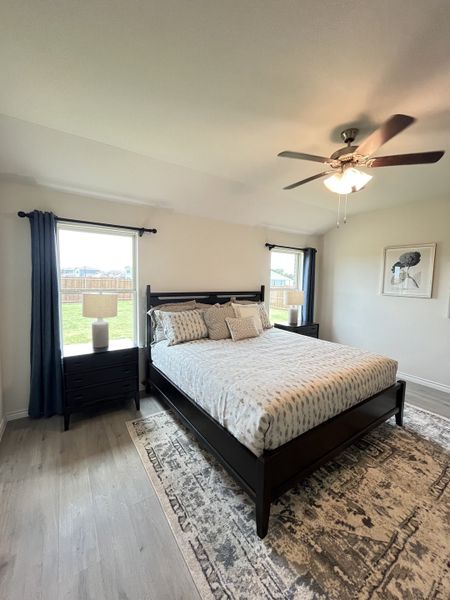 A cozy bedroom featuring a chic dark wood bed, patterned rug, and ample natural light.