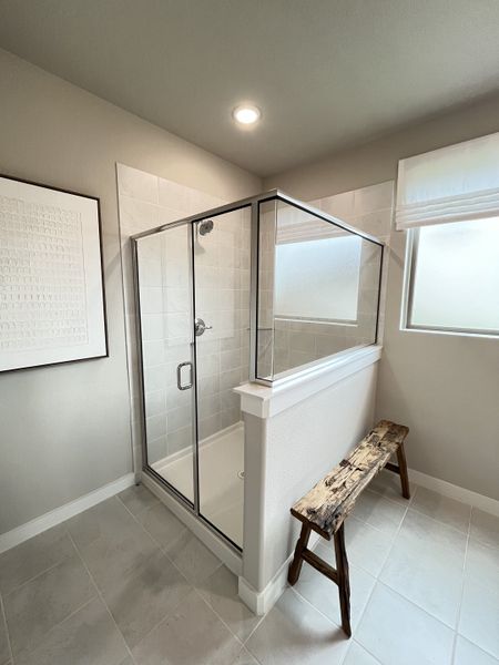 A sleek bathroom with a modern glass shower, neutral tiles, rustic wooden bench, and stylish framed wall art.