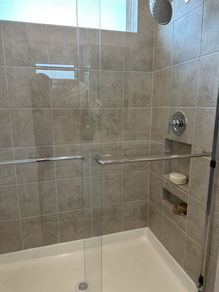 A modern shower with beige tiles, glass doors, and chrome fixtures, featuring built-in shelving and natural lighting. A modern shower with beige tiles, glass doors, and chrome fixtures, featuring built-in shelving and natural lighting.