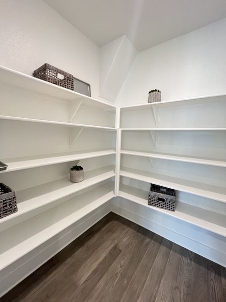A spacious white pantry with ample shelving and elegant wood flooring.