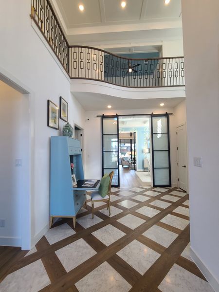 A grand foyer featuring geometric flooring, a stylish turquoise desk, and an elegant staircase with artistic railing. A grand foyer featuring geometric flooring, a stylish turquoise desk, and an elegant staircase with artistic railing.