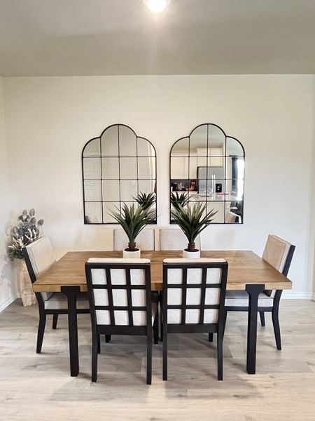 A modern dining room featuring a wooden table, upholstered chairs, and two large, decorative mirrors on a neutral wall.