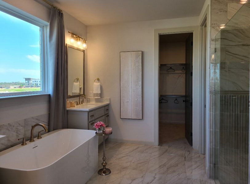 A luxurious bathroom with a freestanding tub, elegant vanity, marble flooring, and a large window offering ample natural light.