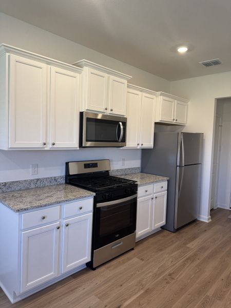 A modern kitchen with sleek white cabinets, granite countertops, stainless steel appliances, and stylish wood flooring.