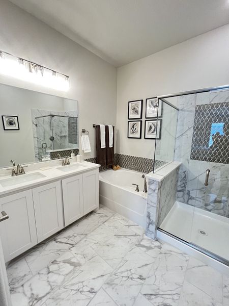 A sleek bathroom with marble flooring, a glass shower, double vanity, and elegant wall art.