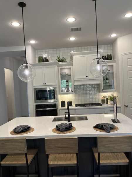 A modern kitchen with sleek white cabinetry, tile backsplash, and a chic island with globe pendant lights. A modern kitchen with sleek white cabinetry, tile backsplash, and a chic island with globe pendant lights.