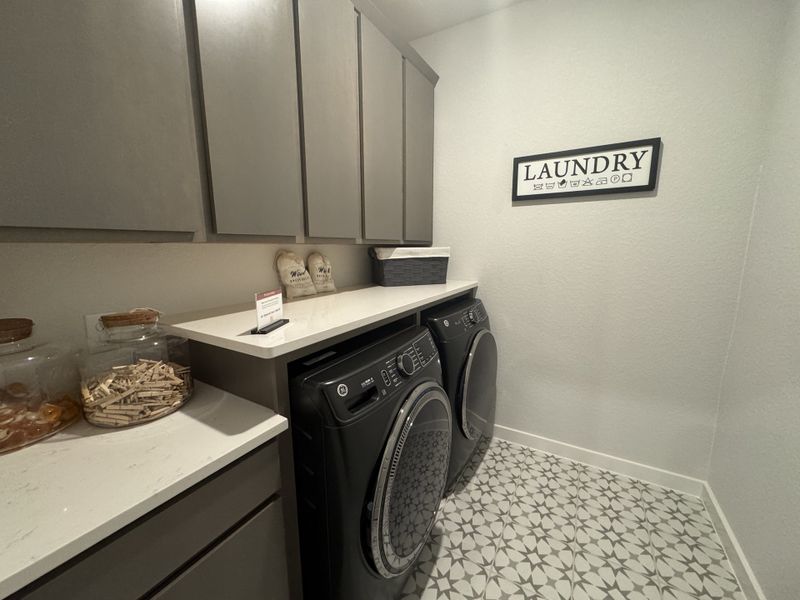 A modern laundry room with sleek grey cabinets, decorative tiles, and a stylish black washer and dryer setup. A modern laundry room with sleek grey cabinets, decorative tiles, and a stylish black washer and dryer setup.