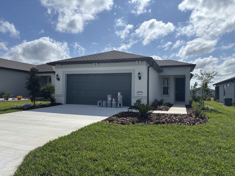 A modern single-story home with a gray garage, lush lawn, and manicured landscaping in Del Webb Stone Creek by Del Webb (Ocala, FL).