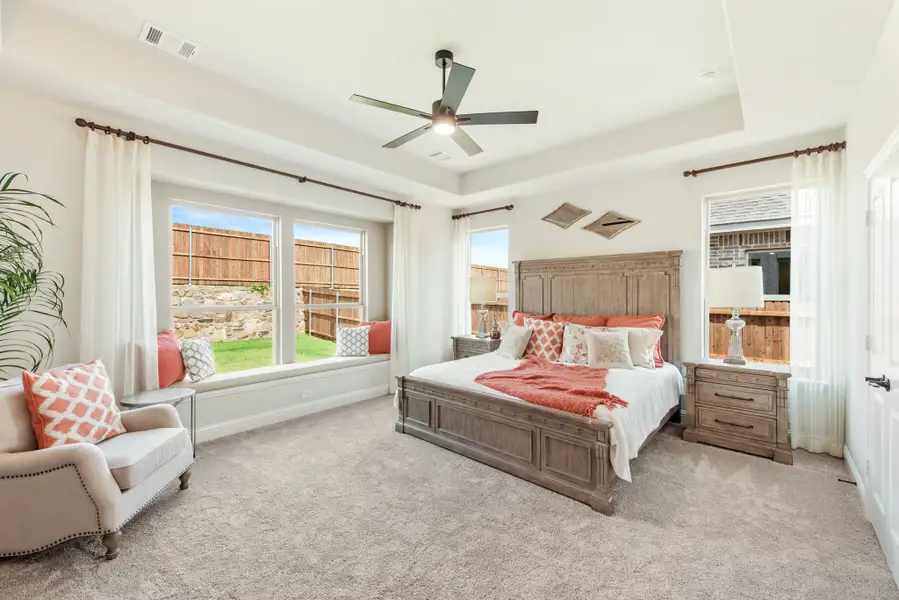 Master bedroom with wood bed frame, tray ceiling, ceiling fan, window seat, and carpet flooring