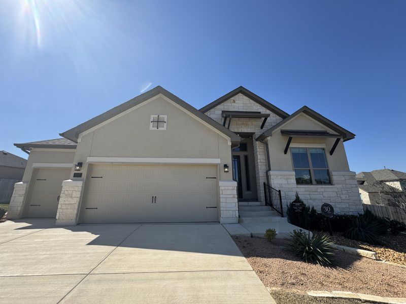 A modern stone-accented home with a spacious driveway in Ventana: 70's by Monticello Homes (Bulverde, TX).