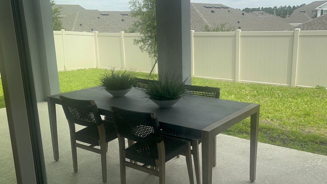 A cozy patio featuring a sleek dining set, potted plants, and a fenced grassy yard, perfect for relaxation and outdoor dining.