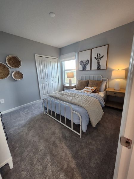 A cozy bedroom with gray walls, elegant artwork, and stylish decor. Features soft carpeting and a bright window view.