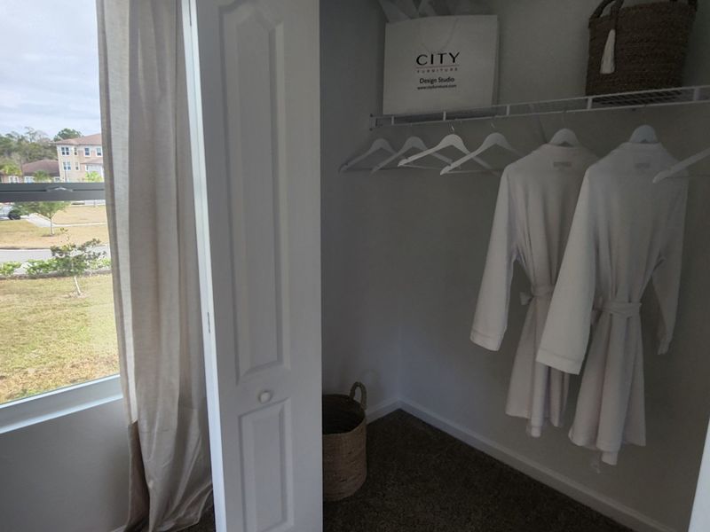 A neat closet with plush robes and a woven basket, adjacent to a window offering natural light.