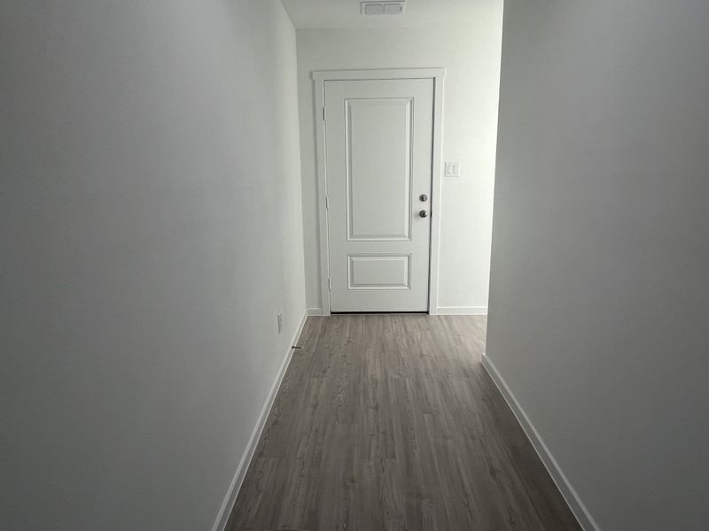 A minimalist hallway with light wood flooring and a white front door, offering a clean and modern entrance.