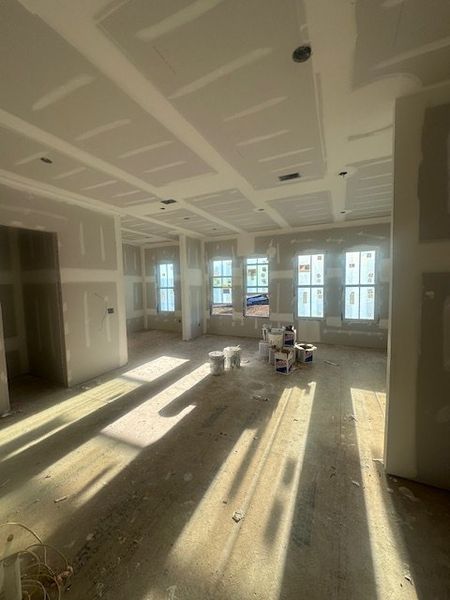 A sunlit room under construction with large windows and drywall, showcasing potential for open, airy interiors.