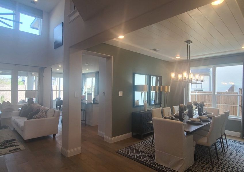 A spacious living and dining area with high ceilings, modern chandelier, and elegant decor, bathed in natural light.