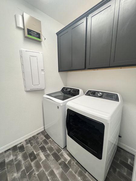 A modern laundry room with sleek gray cabinets, white washer and dryer, and stylish dark tile flooring.