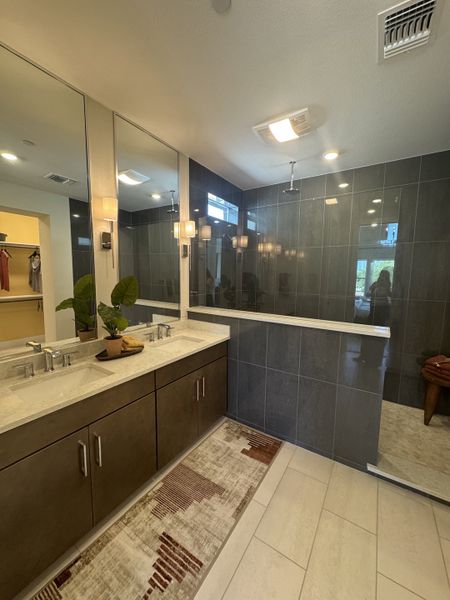 A modern bathroom with dual sinks, a sleek vanity, floor-to-ceiling mirror, and a spacious glass-enclosed shower.
