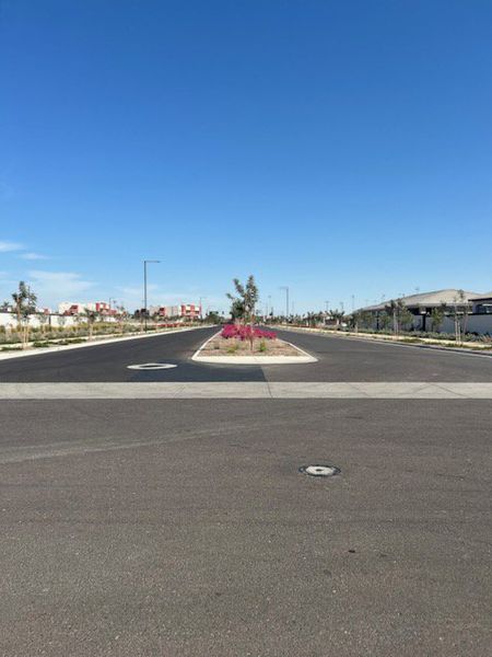 A welcoming street with landscaped medians and clear skies in Avion: Arbor by Lennar (Goodyear, AZ).