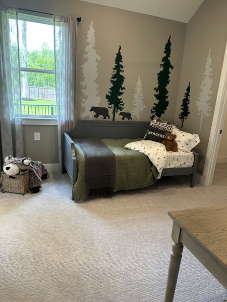A cozy bedroom with woodland-themed wall art, a gray daybed, and plush toys, creating a delightful retreat for kids.