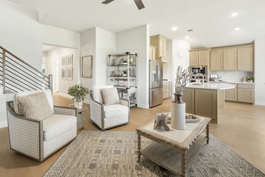 Open-concept living area with two accent chairs and wood floors flowing into kitchen with tan cabinets and island