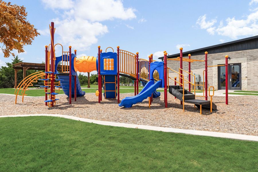 Community playground with blue and orange play structure, slides, and climbing equipment on wood chip surface