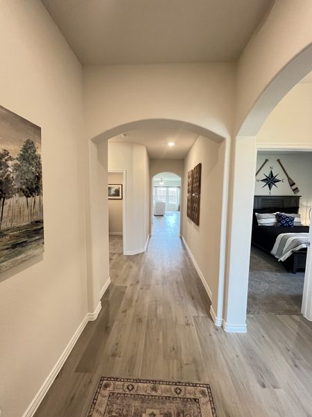 A welcoming hallway with light wood floors, archways, and elegant decor leads to a sunlit room, creating an open and airy feel. A welcoming hallway with light wood floors, archways, and elegant decor leads to a sunlit room, creating an open and airy feel.