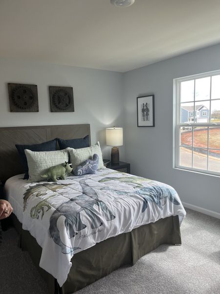 A cozy bedroom with dinosaur-themed bedding, soft lighting, and a large window offering natural light. A cozy bedroom with dinosaur-themed bedding, soft lighting, and a large window offering natural light.