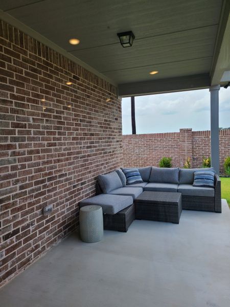A cozy patio with a brick wall, gray sectional sofa, and a view of the green backyard, perfect for relaxation.