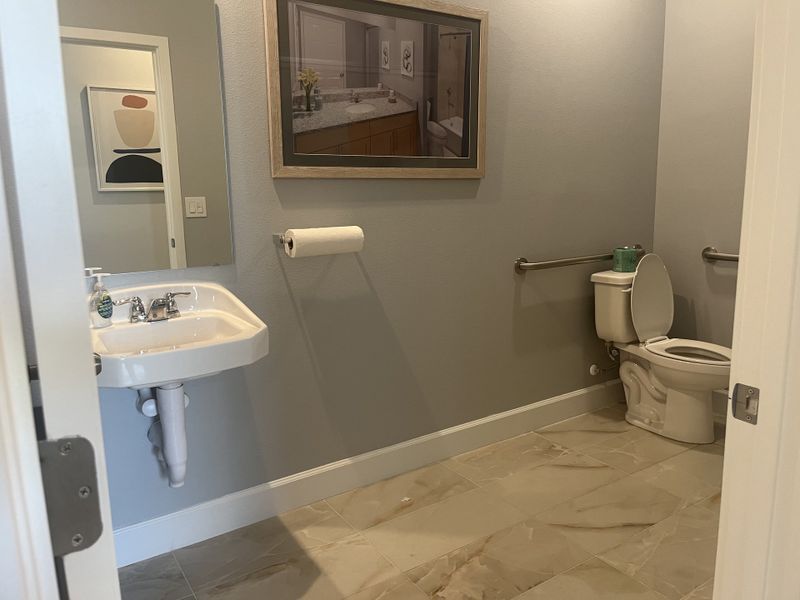 A modern bathroom with a pedestal sink, safety bars, and neutral-toned tiles for a sleek, accessible design.