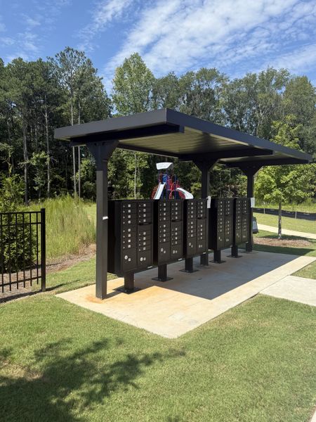 A modern outdoor mailbox pavilion with lush greenery in Campground Crossing by Dream Finders Homes (Mcdonough, GA). A modern outdoor mailbox pavilion with lush greenery in Campground Crossing by Dream Finders Homes (Mcdonough, GA).