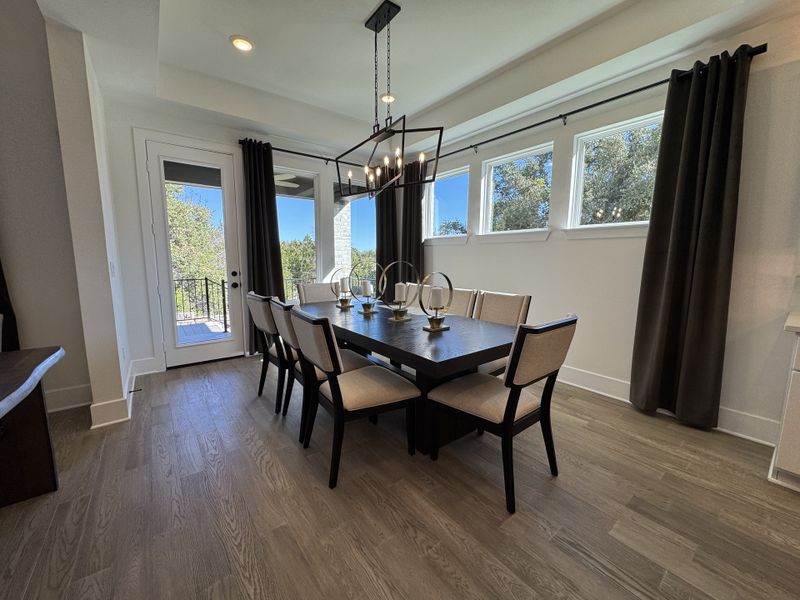 A contemporary dining room with elegant lighting, large windows, and a wooden table set for six, offering scenic outdoor views.